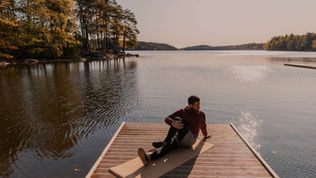 Man sitting on a wooden dock by a calm lake, autumn trees glowing in warm light, with a peaceful mood.