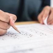 A hand using a pencil to fill in bubbles on a standarized test sheet