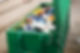 A green dumpster filled with various discarded plastic containers and jugs