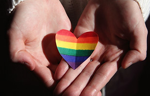 hands carefully holding a paper heart with lgbt flag pride colors