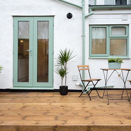 A general exterior view of a back garden patio area with wood decking, potted plants, Drag