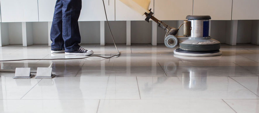 Cleaner running a floor polishing machine across a tiled lobby — office cleaning schedule