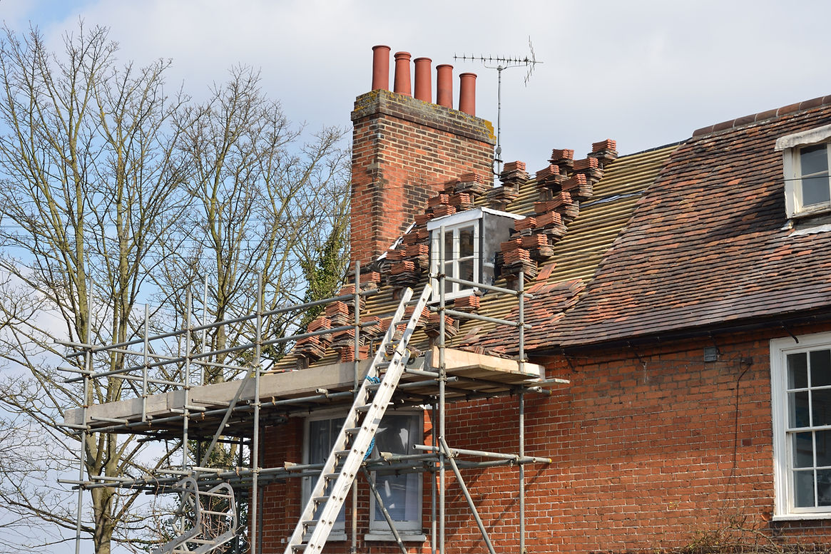 Scaffolding surrounds a red brick house with a damaged roof undergoing repairs
