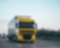 A bright yellow cargo truck drives quickly on a highway,