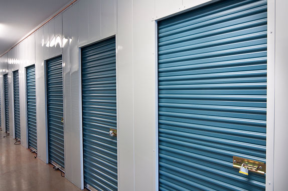 A row of closed blue storage unit doors with white frames in a clean, well-lit facility