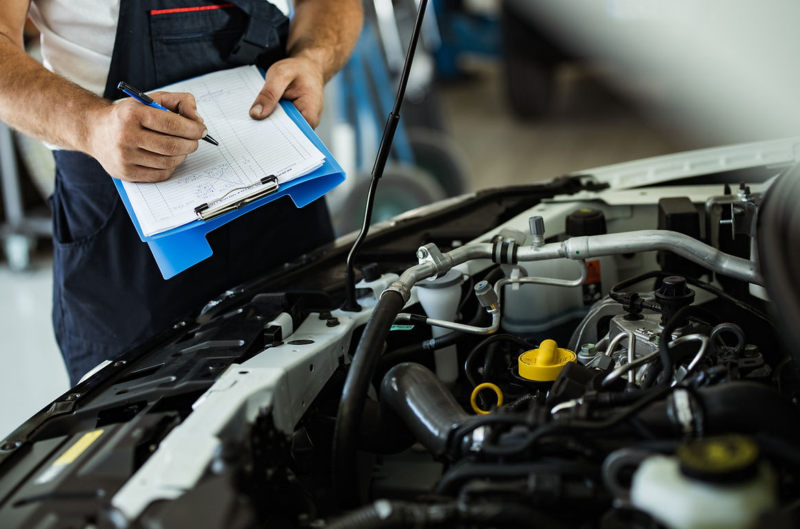 A man examines a car engine while holding a clipboard, assessing its condition or taking notes