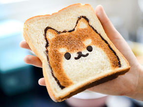 Toast with a cute dog face design in chocolate held by a hand. Bright kitchen setting, cheerful and playful mood.