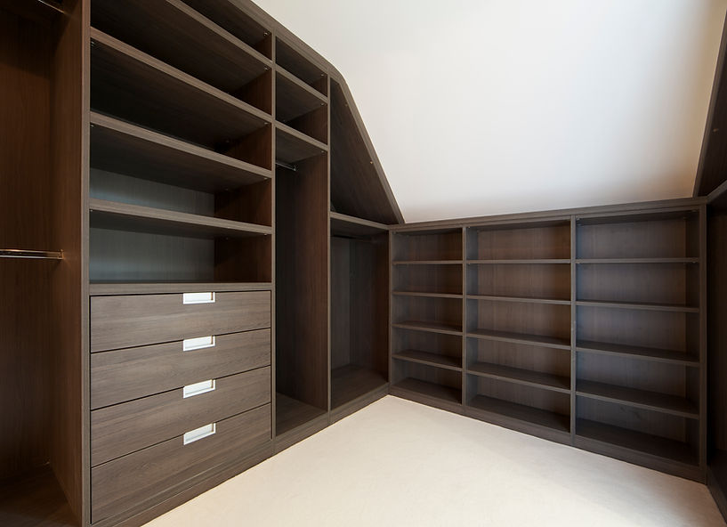 Spacious walk-in closet with dark wooden shelves and drawers under a sloped ceiling