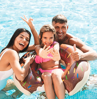 Family in Pool with child on rubber dingy everyone is laughing and the water is bright blue