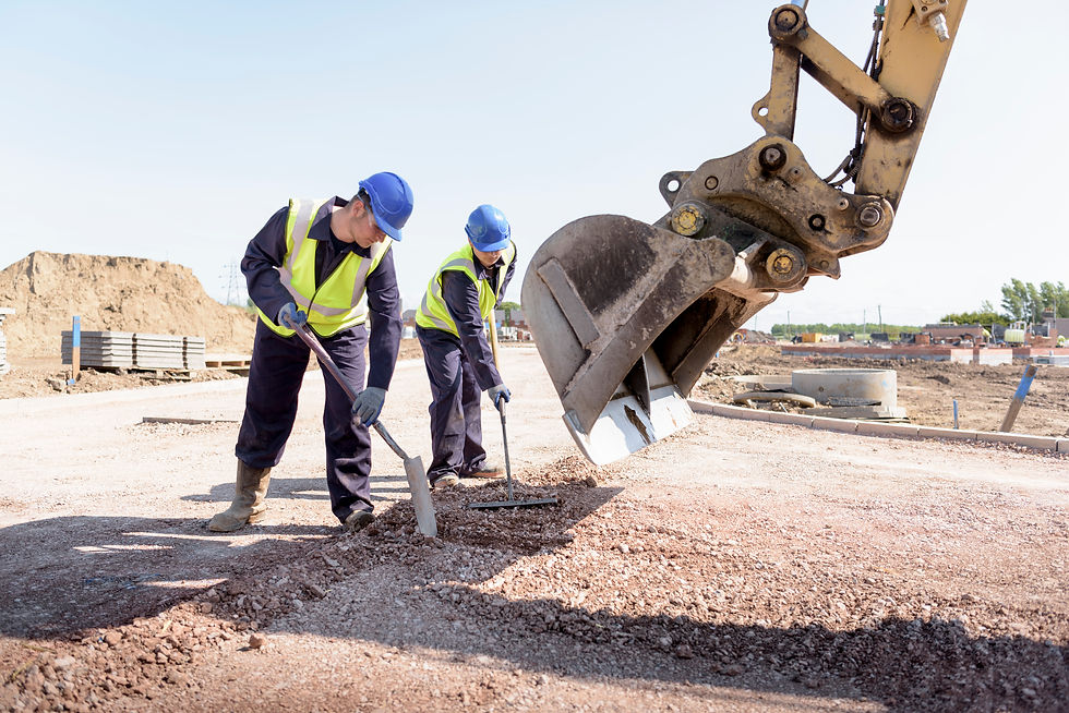 Two construction workers smooth gravel near a large excavator