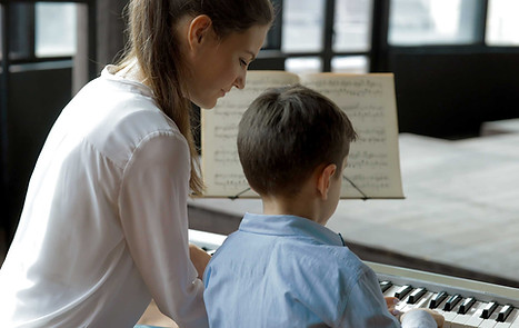 An adult and a child sitting at a keyboard piano for a piano lesson
