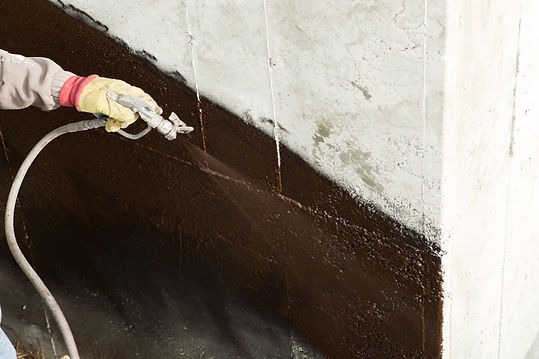 A worker is spraying waterproof sealant on a new home's concrete foundation.