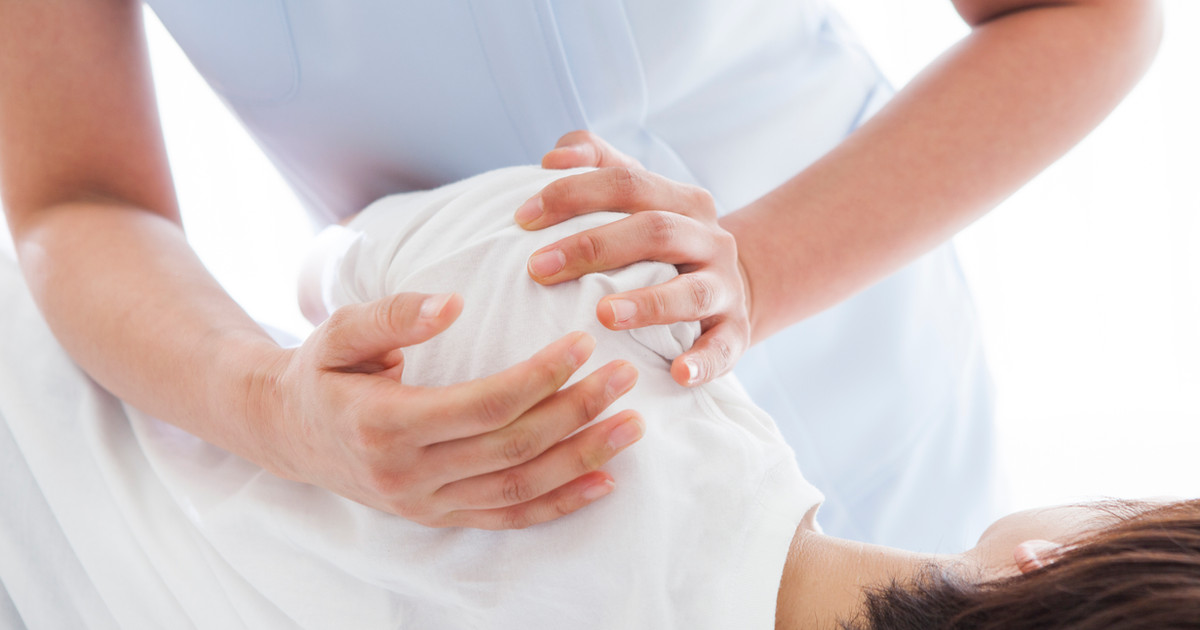 An osteopath assessing a person's posture and movement before beginning hands-on treatment in a clinical setting.