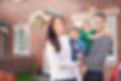 A young family stand proudly outside their house. Mother and father are holding a young dad
