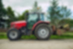 Side view of a red tractor with a rear sweeper attachment on a rural path