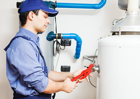 A uniformed plumber working on a hot water heater with an adjustable spanner.