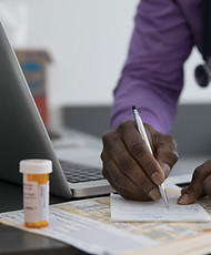 Male doctor writing prescription at laptop in clinic examination room