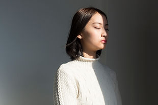 A content young woman is looking to the side at something off camera, their body half bathed in sun and half in light shadow.