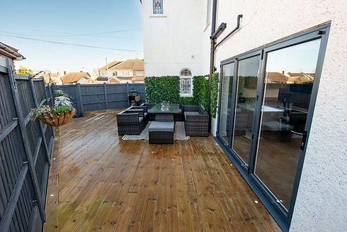 Polished timber decking patio with dark rattan garden furniture next to modern folding glass doors