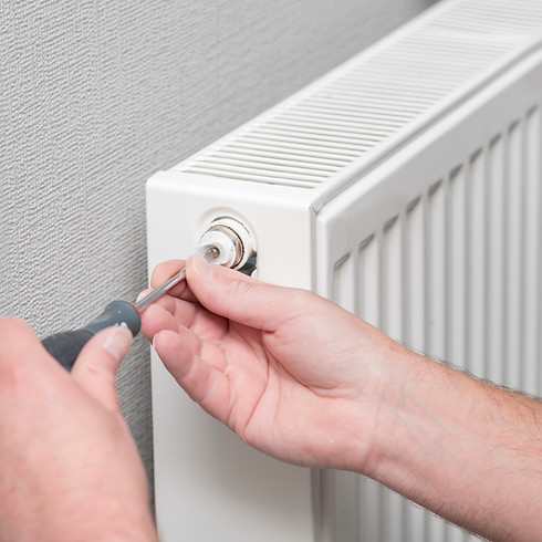 A plumber fixing a radiator valve with a screwdriver