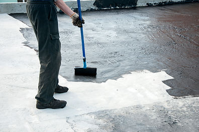 A person applies waterproofing sealant on a flat roof with a long-handled roller