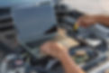A mechanic's hands hold a dipstick, checking oil under a car hood with a laptop nearby