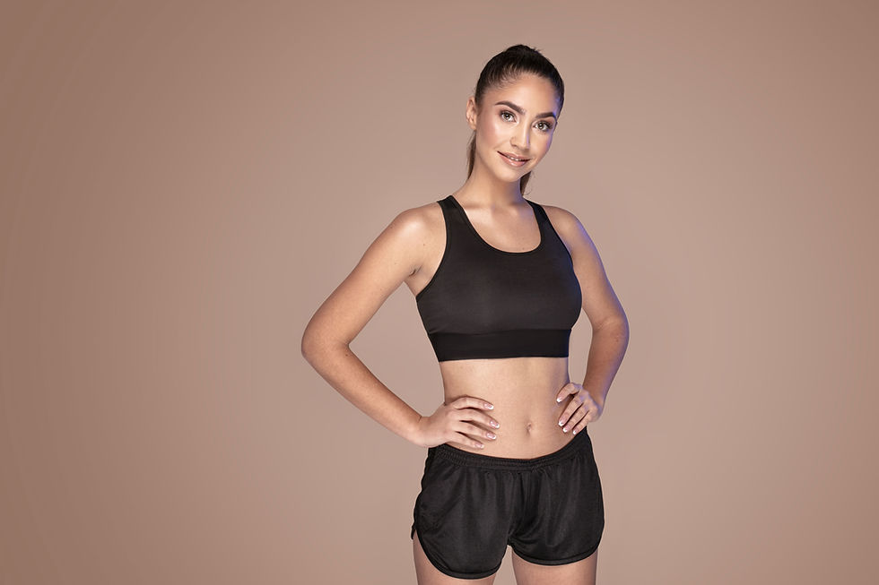 Smiling woman in black sports bra and shorts with hands on hips. Active wear.