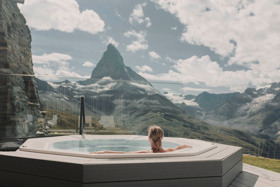 Hot tub with steam rising in snowy mountain landscape. Sun shines over frosted trees, creating a serene winter scene.
