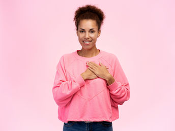 I woman with a smile on her face holds her hands to her heart.