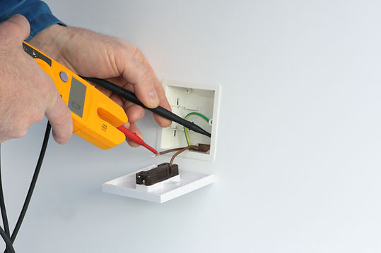 Electrician testing white wall socket outlet with yellow voltage meter probe