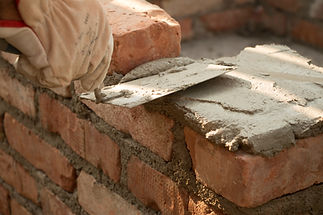 A gloved hand uses a trowel to apply mortar to a brick wall
