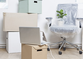 Stack of cardboard boxes, a wrapped swivel chair and a notebook in an office
