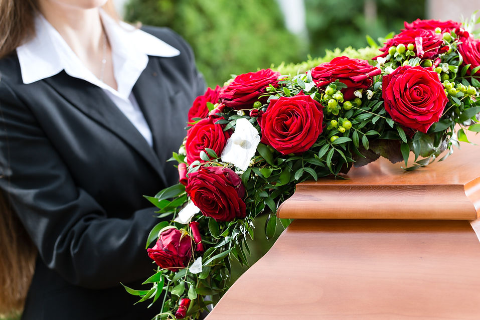 Mourning woman during funeral with red rose standing at casket or coffin