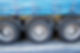 Close-up of three large truck wheels on asphalt, partially covered by a blue tarp with straps