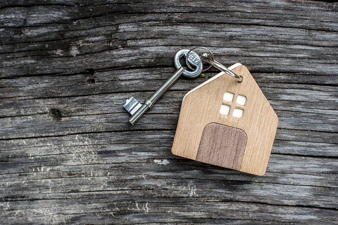 key with shaped house keychain on chain on wood texture background. Idea: buying a house,