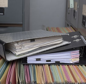 A stack of binders and file folders filled with colorful tabbed documents.