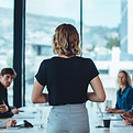 Mulher de frente para uma mesa com pessoas sentadas