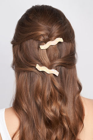 The back of a head with styled wavy brown hair adorned with gold hair clips.