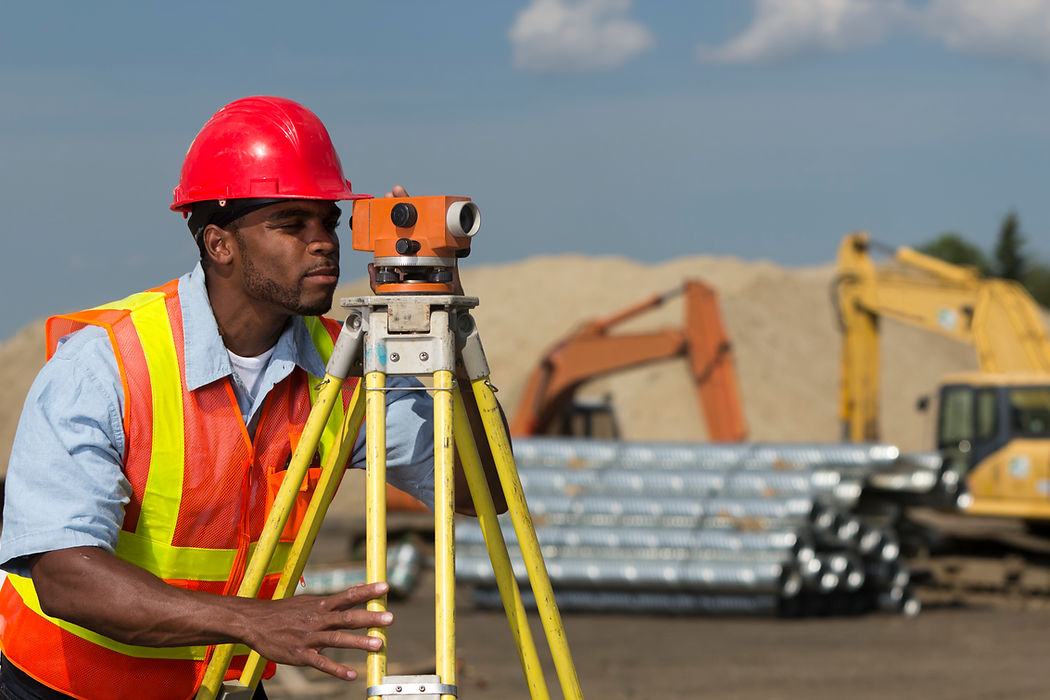 A construction worker in a red hard hat uses a surveying instrument on a job site