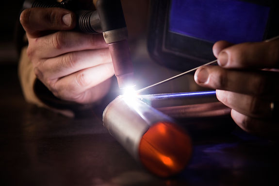 Hands holding a welding torch and rod work on a metal cylinder