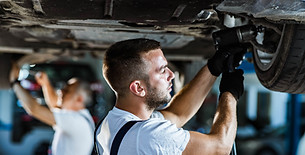 Young auto mechanic changing tire while standing under the chassis of a car in a workshop