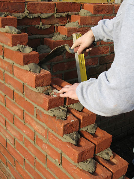 A person laying bricks on a wall, smoothing gray mortar with their hand