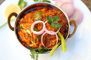 A close up of a rich chicken curry garnished with fresh onion rings and green chillies