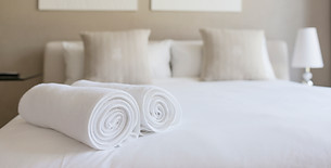 Two rolled white bath towels placed neatly on a freshly made hotel bed