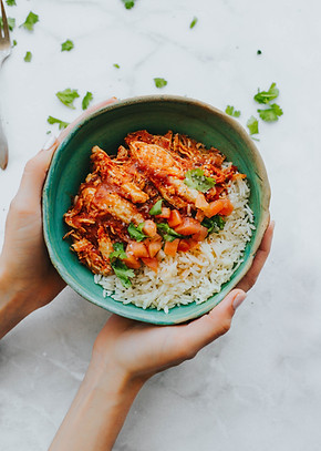 Hands holding a bowl with tomato chicken curry and rice