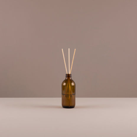Bottiglia di vetro con bastoncini di legno su sfondo neutro, diffusore.