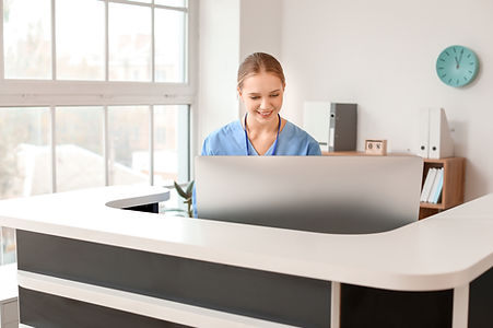 Young woman at a front desk in a medical office with a caring smile on her face.