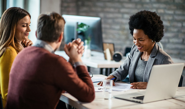 A business meeting between 3 individuals. Two are Caucasian and one is Black. They're looking over papers on the table.