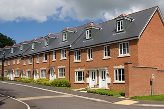 A row of modern red brick townhouses with slate roofs under a partly cloudy sky