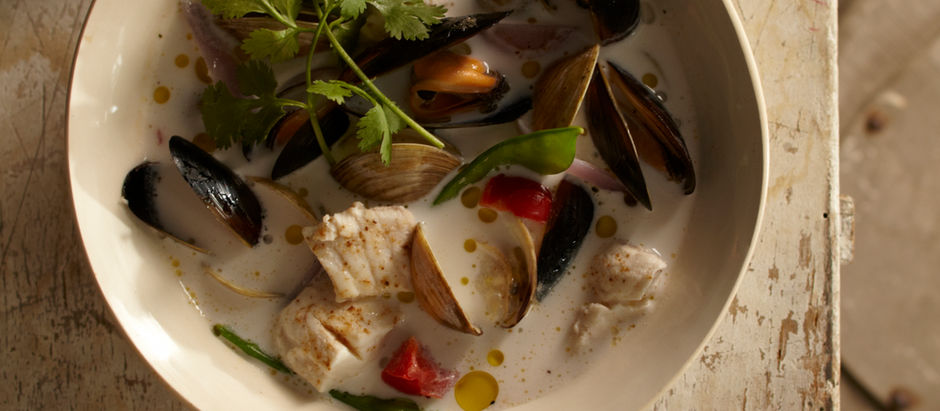 A bowl of Filipino seafood soup featuring mussels, white fish, snow peas, and red bell pepper in a creamy coconut broth, served hot and garnished with fresh herbs.